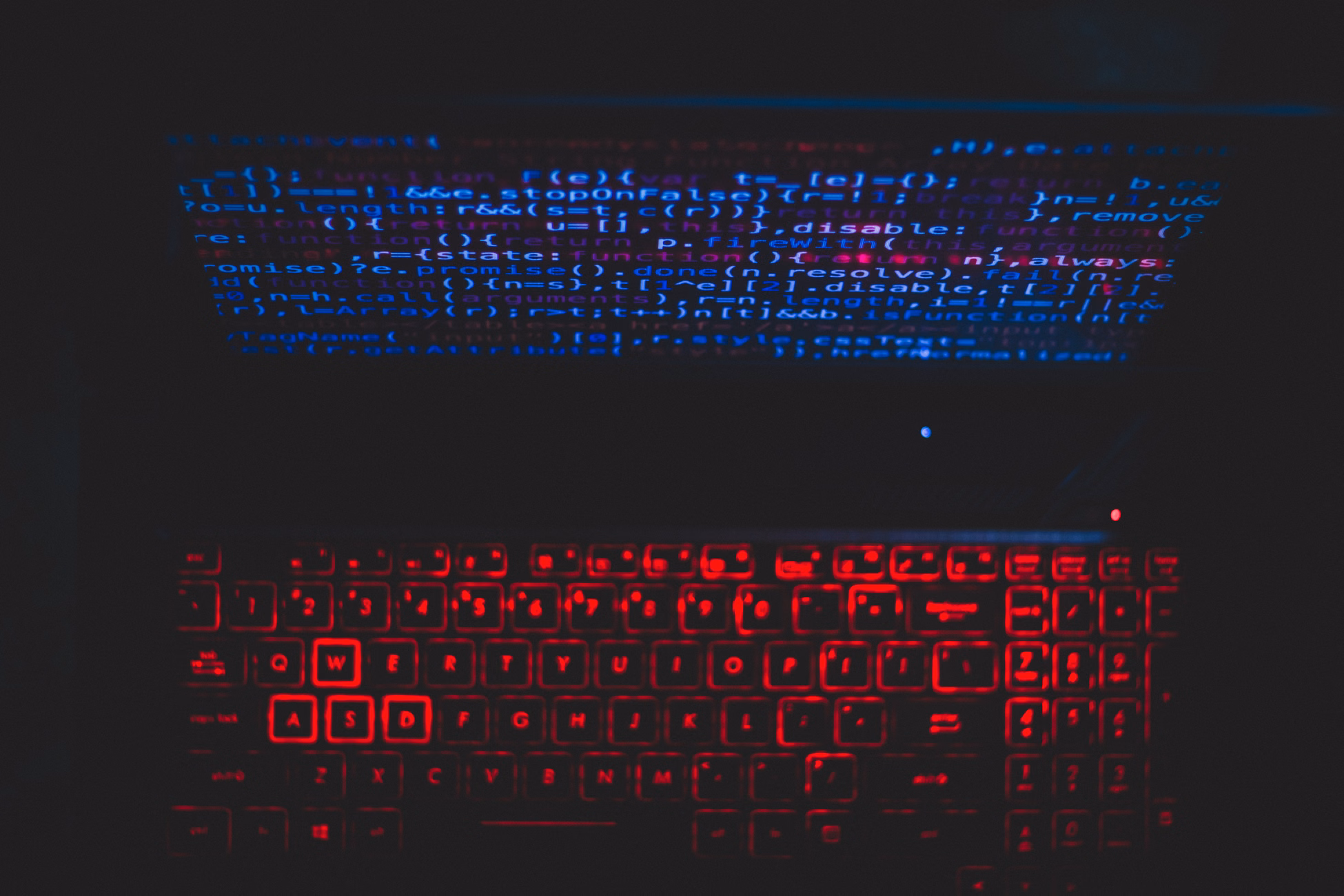 Dark-themed laptop setup with a red glowing keyboard and code on screen, ideal for tech enthusiasts.
