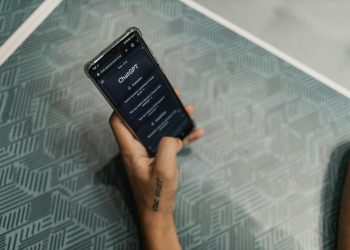 Close-up of a person holding a smartphone displaying the ChatGPT application interface on a patterned table.