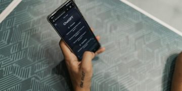 Close-up of a person holding a smartphone displaying the ChatGPT application interface on a patterned table.