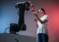 A woman and a robot arm collaboratively holding a flower, symbolizing technology's gentle touch.