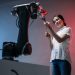 A woman and a robot arm collaboratively holding a flower, symbolizing technology's gentle touch.