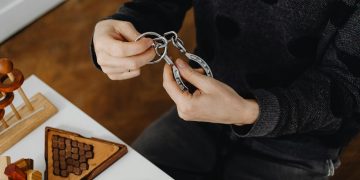 Top view of hands solving metal puzzle, surrounded by wooden brain teasers on a table.