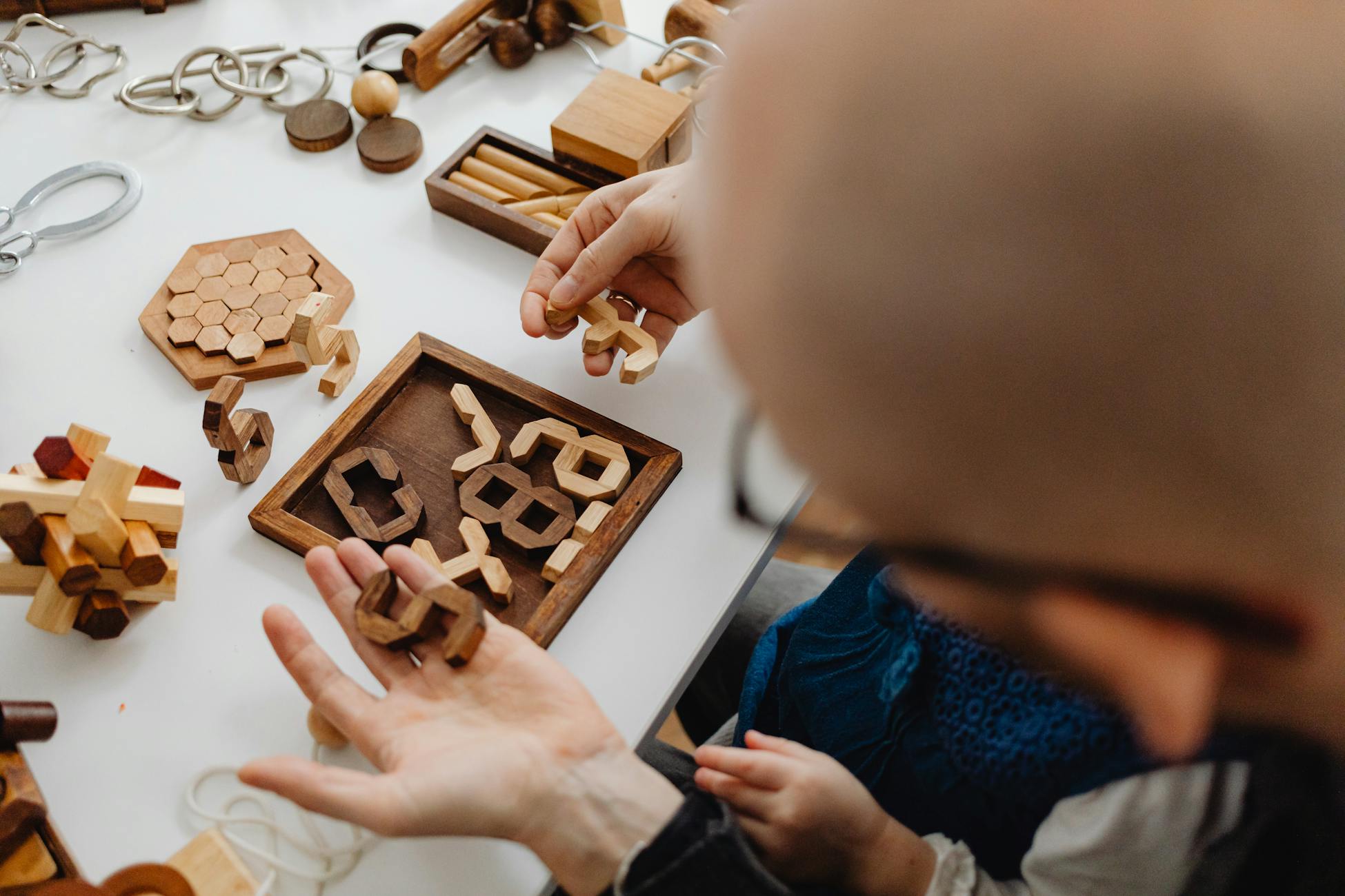 Adults and children playing with intricate wooden puzzles on a white table, fostering creativity.