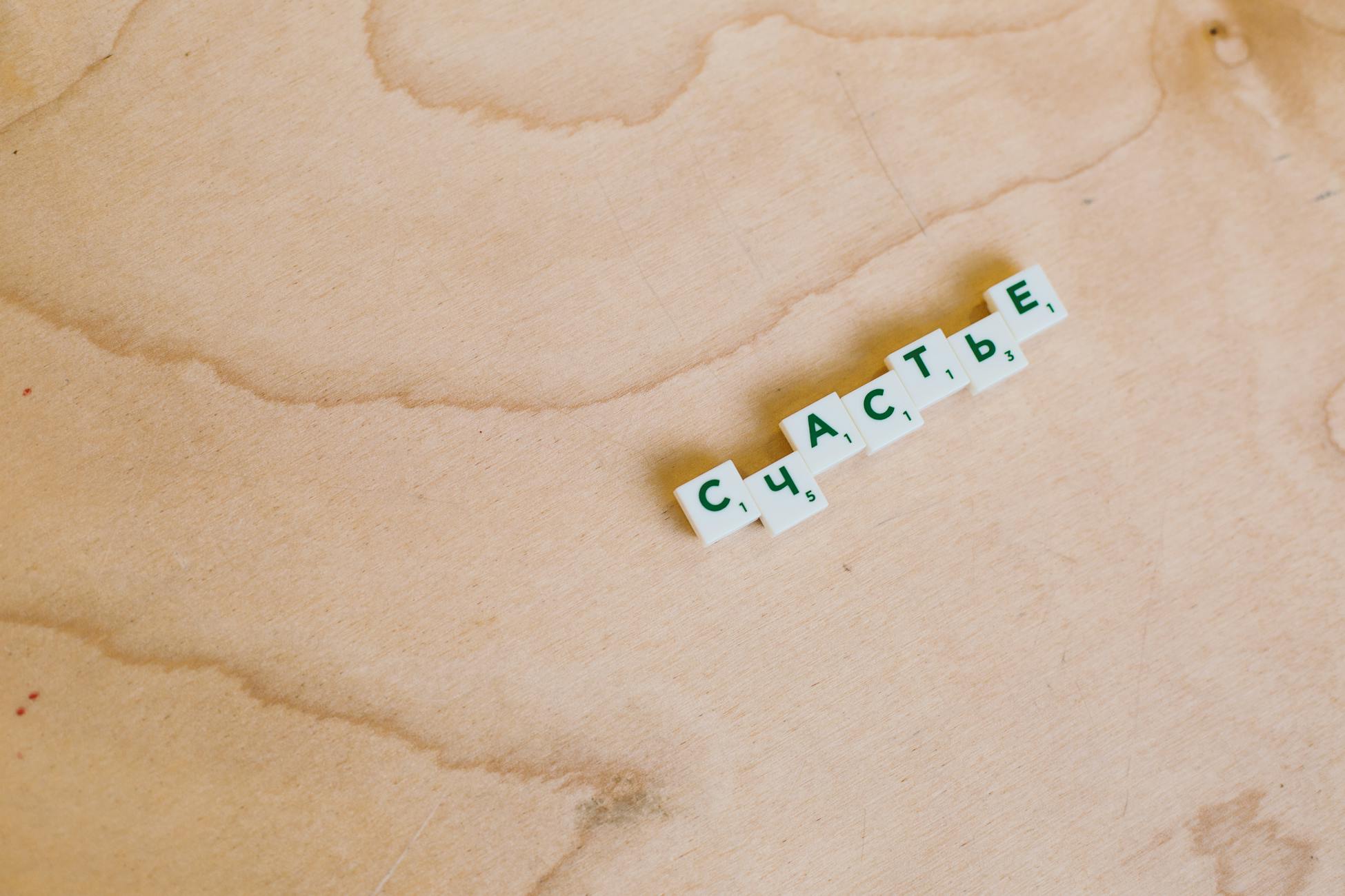 Cyrillic Scrabble tiles spelling 'happiness' on a wooden board.