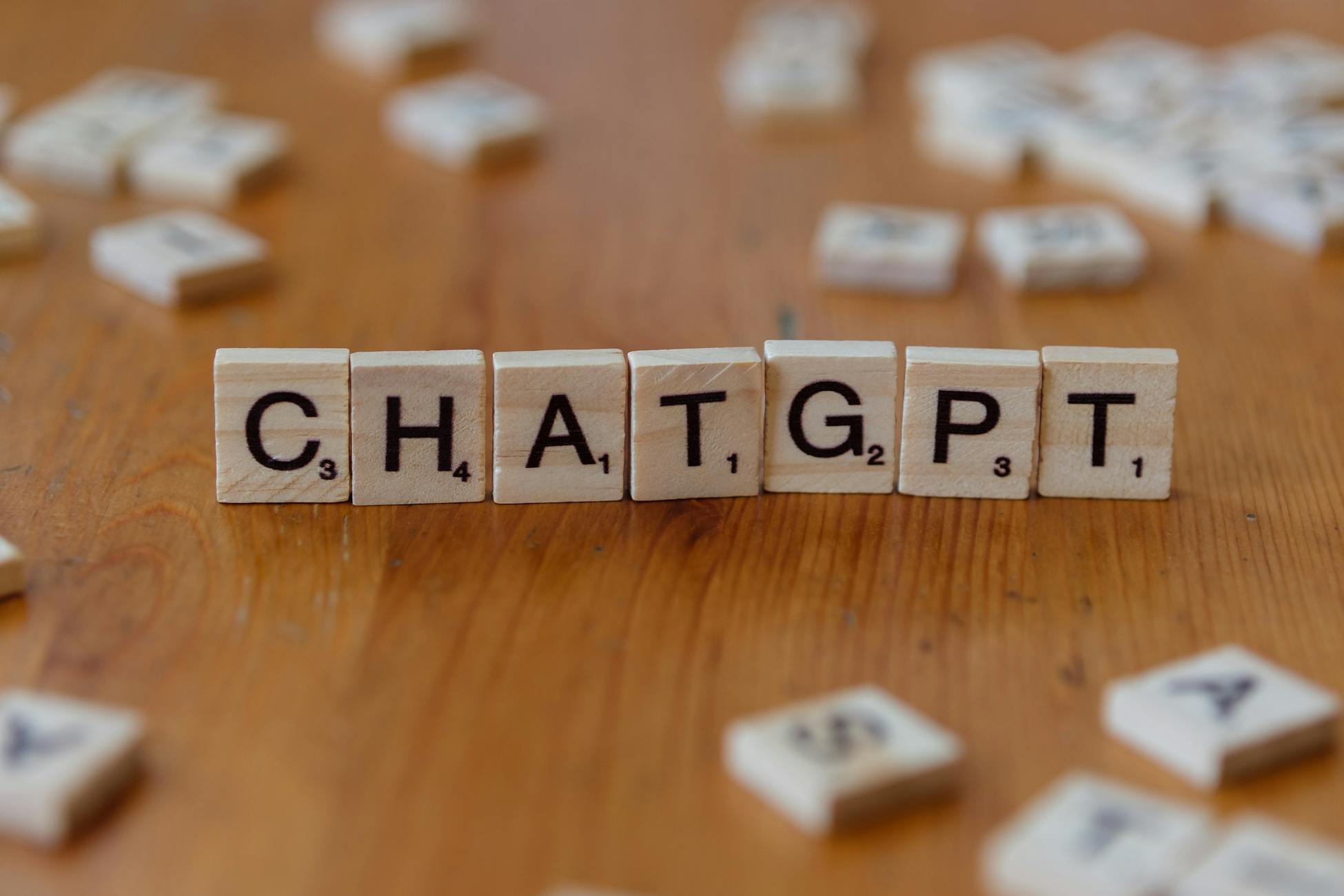 Scrabble tiles spelling 'CHATGPT' on wooden surface, emphasizing AI language models.