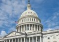 A striking view of the US Capitol dome with flag and blue sky in Washington, DC.