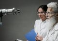 Two scientists wearing lab coats and goggles analyzing a robotic arm in a laboratory setting.
