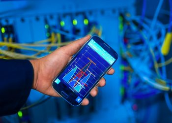Hand holding smartphone displaying network analysis in high-tech server environment.