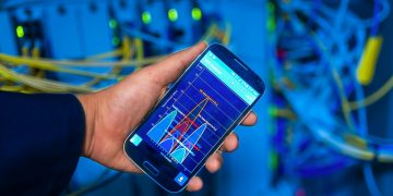 Hand holding smartphone displaying network analysis in high-tech server environment.