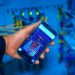 Hand holding smartphone displaying network analysis in high-tech server environment.