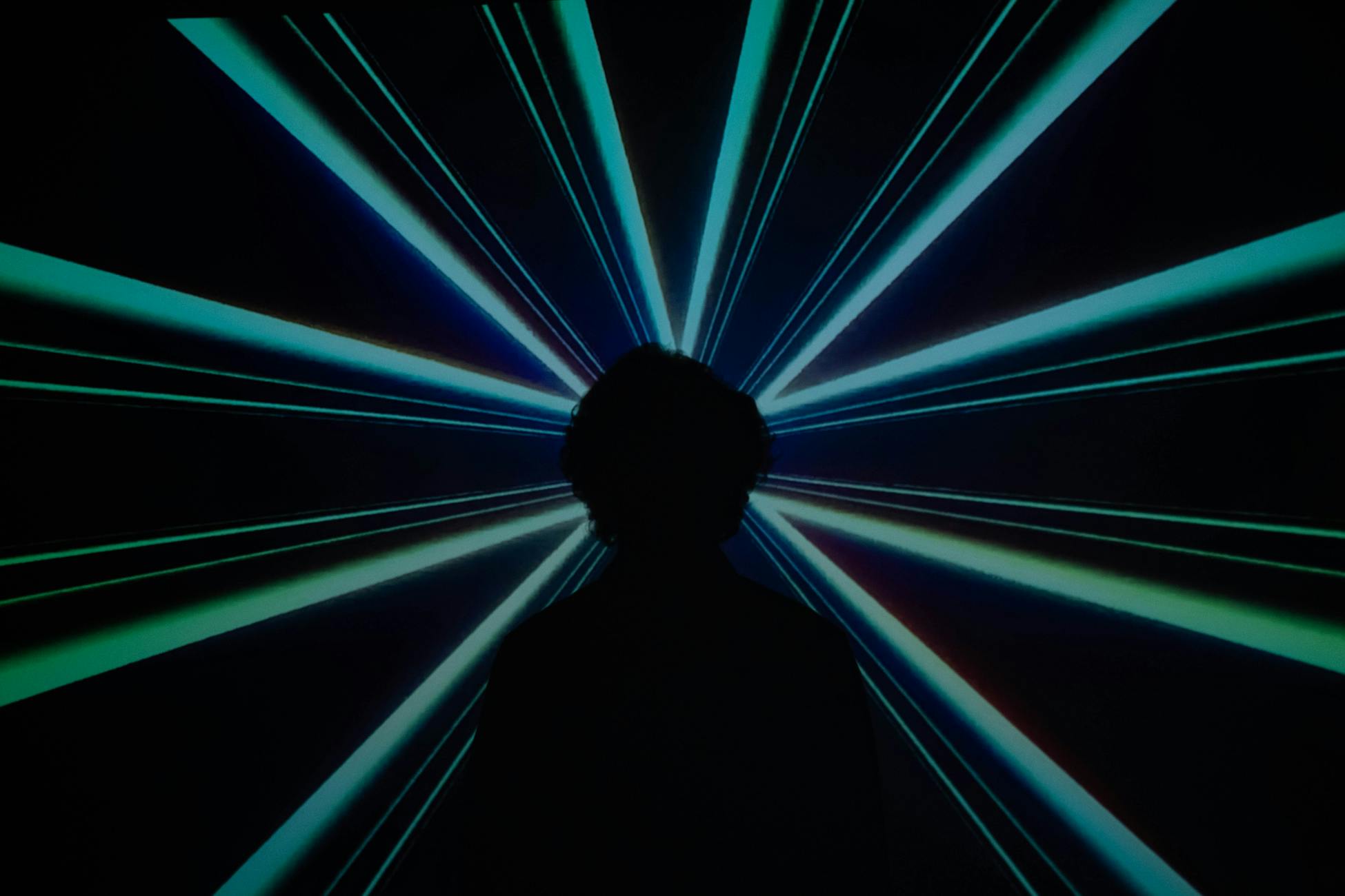 Silhouette of a person in front of a dynamic and colorful laser light display.