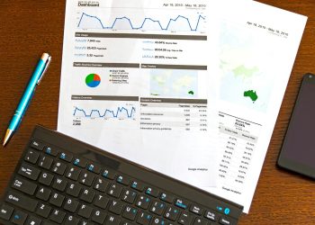 Flatlay of a business analytics report, keyboard, pen, and smartphone on a wooden desk.
