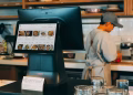 Digital ordering system in a restaurant kitchen with a touchscreen display and a chef at work.
