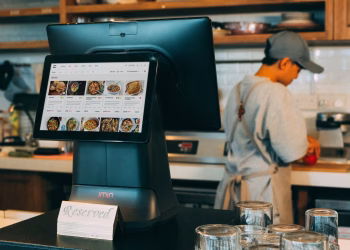 Digital ordering system in a restaurant kitchen with a touchscreen display and a chef at work.