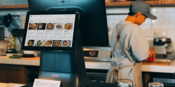 Digital ordering system in a restaurant kitchen with a touchscreen display and a chef at work.