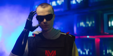 Portrait of an individual in futuristic gear, featuring a prosthetic arm and sunglasses.