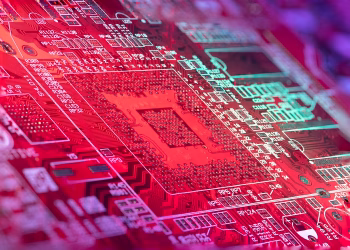 Red printed board of digital device with bright electric circuit with numbers and symbols placed in room on blurred background
