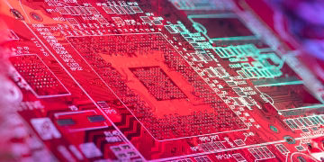 Red printed board of digital device with bright electric circuit with numbers and symbols placed in room on blurred background