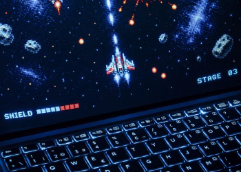 A classic arcade space shooter game displayed on a laptop with illuminated keyboard, showing retro graphics.