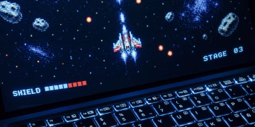 A classic arcade space shooter game displayed on a laptop with illuminated keyboard, showing retro graphics.