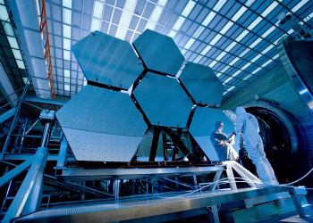 Engineers in protective suits work on telescopic mirrors in a high-tech lab.