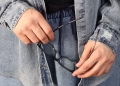 Person in denim outfit holding eyeglasses, showcasing casual fashion and style.