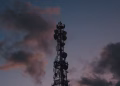 Silhouette of a telecommunications tower against a vibrant twilight sky with clouds.