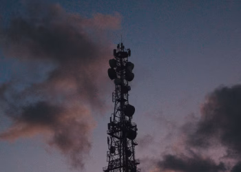 Silhouette of a telecommunications tower against a vibrant twilight sky with clouds.