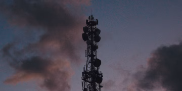 Silhouette of a telecommunications tower against a vibrant twilight sky with clouds.