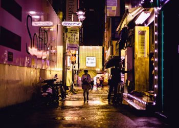 Explore Tokyo's vibrant nightlife captured in a glowing, rain-soaked alleyway, showcasing urban charm and colorful street lights.