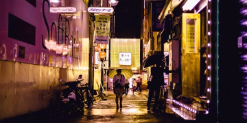 Explore Tokyo's vibrant nightlife captured in a glowing, rain-soaked alleyway, showcasing urban charm and colorful street lights.