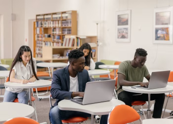 Students focused on laptops and notes in a bright classroom setting.