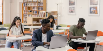 Students focused on laptops and notes in a bright classroom setting.