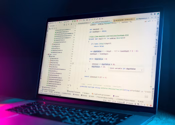 A laptop screen showing a code editor with visible programming code in a dimly lit environment.