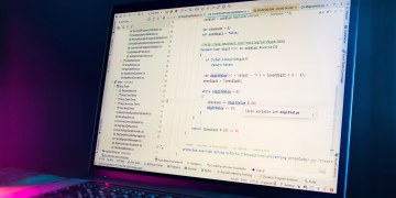 A laptop screen showing a code editor with visible programming code in a dimly lit environment.
