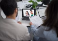 Two professionals conduct a virtual job interview using laptops in a modern office.