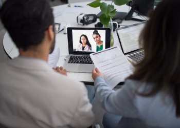 Two professionals conduct a virtual job interview using laptops in a modern office.
