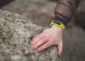 Close-up of a hand with a fitness tracker touching a rock outdoors, showcasing exploration.