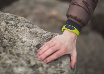 Close-up of a hand with a fitness tracker touching a rock outdoors, showcasing exploration.