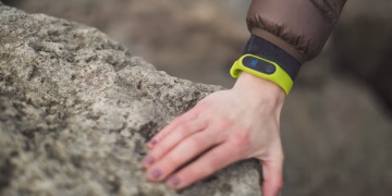 Close-up of a hand with a fitness tracker touching a rock outdoors, showcasing exploration.
