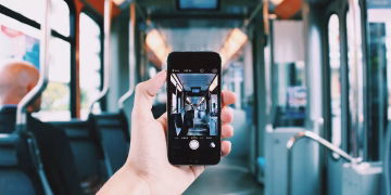A hand holds a smartphone, capturing the interior of a train, creating a unique visual perspective.