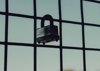 Close-up of a steel padlock on a mesh fence, symbolizing protection and security.