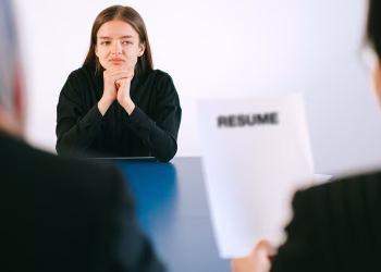 A woman in a job interview facing two employers with a focus on her resume.