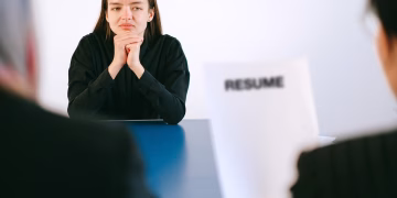 A woman in a job interview facing two employers with a focus on her resume.