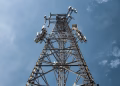 A low-angle shot of a tall metal communications tower with multiple antennas against a clear blue sky.