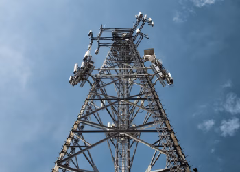 A low-angle shot of a tall metal communications tower with multiple antennas against a clear blue sky.