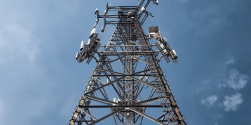 A low-angle shot of a tall metal communications tower with multiple antennas against a clear blue sky.