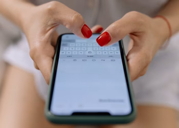 Close-up image of hands with red nails typing on a smartphone screen, showcasing modern technology.