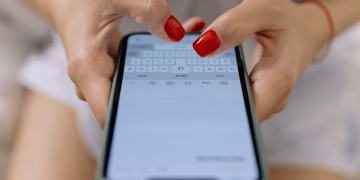 Close-up image of hands with red nails typing on a smartphone screen, showcasing modern technology.