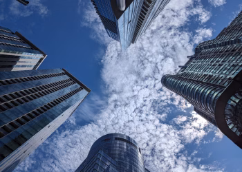 Looking up at modern skyscrapers under a blue sky with dramatic clouds.